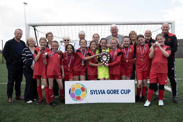 Millbrook Primary in all red kits. all players and coaches together celebrating their win with the trophy