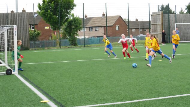 Girl one on one with the goalkeeper about to shoot and score wearing a yellow football top and blue shorts at the Sylvia gore tournament